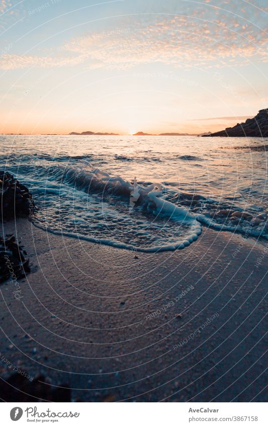 Vertikales Bild einer Flut am Strand über dem Sand während eines farbenprächtigen Sonnenuntergangs mit den Inseln als Hintergrund und Kopierraum Meer Gezeiten