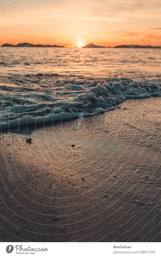 Vertikales Bild einer Flut am Strand über dem Sand während eines farbenprächtigen Sonnenuntergangs mit den Inseln als Hintergrund und Kopierraum Meer Gezeiten