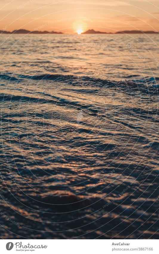 Vertikales Bild einer Flut am Strand über dem Sand während eines farbenprächtigen Sonnenuntergangs mit den Inseln als Hintergrund und Kopierraum Meer Gezeiten