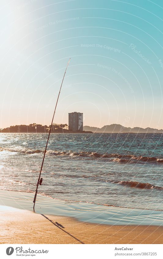 Angelrute an einem Strand vor einem massiven Gebäude während eines Sonnenuntergangs in Spanien Stab Meer Mast Erholung Sport horizontal Rolle Brandung Angler