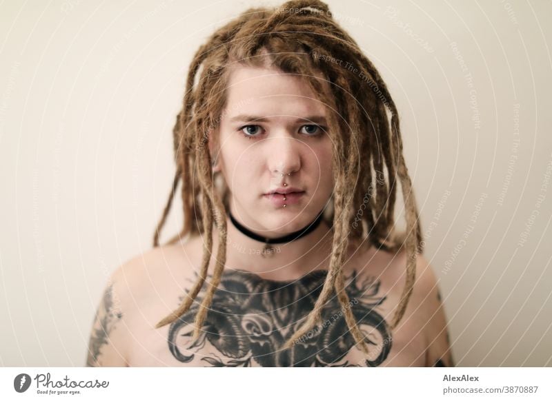 Portrait einer jungen Frau mit Dreadlocks, die eine großflächige Tätowierung eines Ochsenkopfes auf den Dekolletè hat dunkelblond Schmuck Piercing Ohrring