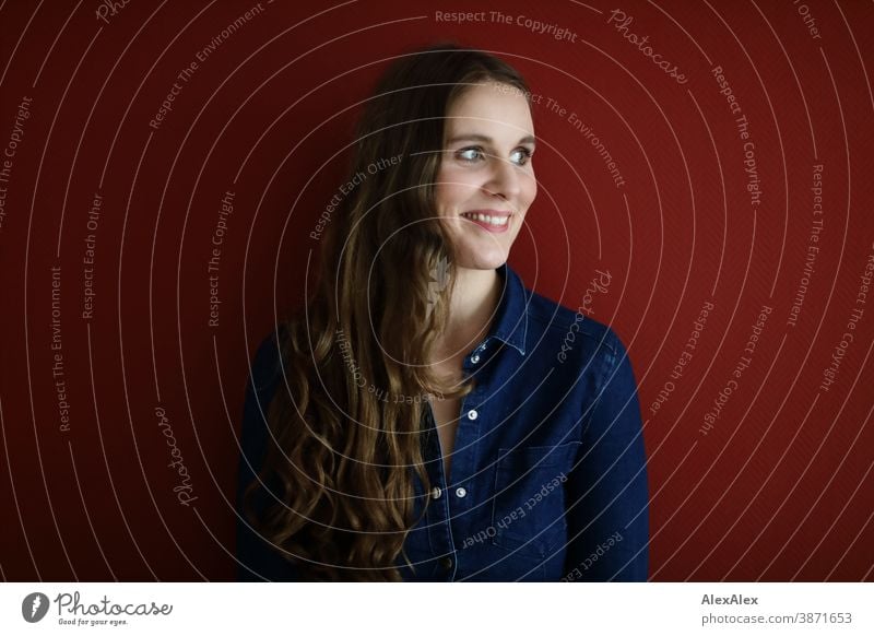 Portrait einer jungen Frau vor einer roten Wand schlank schön brünett lange Haare Schulter Gesicht schlau emotional sehen schauen Blick direkt natürlich