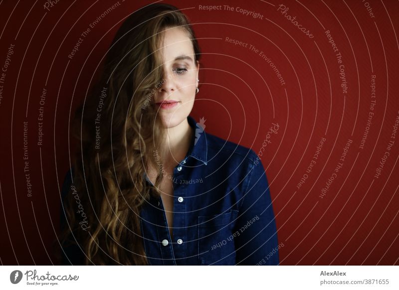 Portrait einer jungen Frau vor einer roten Wand schlank schön brünett lange Haare Schulter Gesicht schlau emotional sehen schauen Blick direkt natürlich