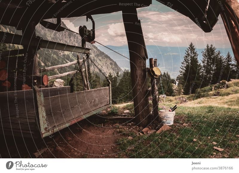 Lastenseilbahn auf der Alm - Ausblick ins Tal der Alpen - Holzunterstand als Schutz vor dem Wetter - der Materialträger für die Versorgung des Bauernhofes im Gebirge ist aus Holz gefertigt