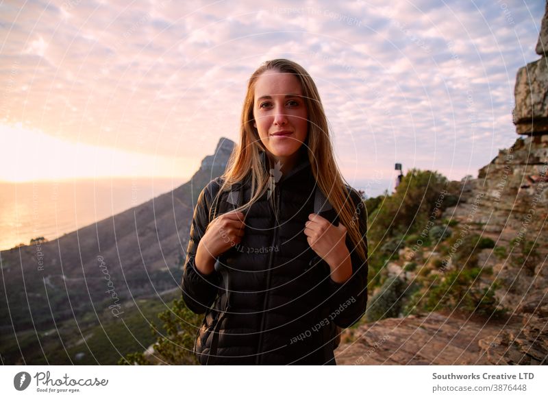 Porträt einer jungen Frau, die entlang des Küstenweges wandert, während die Sonne hinter ihr über dem Meer untergeht Junge Frauen Wanderung wandern Spaziergang