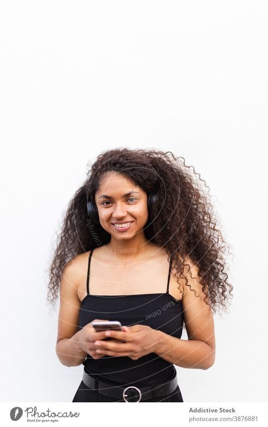 Optimistische schwarze Frau, die auf der Straße Musik hört zuhören Kopfhörer meloman genießen Afro-Look Frisur krause Haare Smartphone ethnisch Afroamerikaner