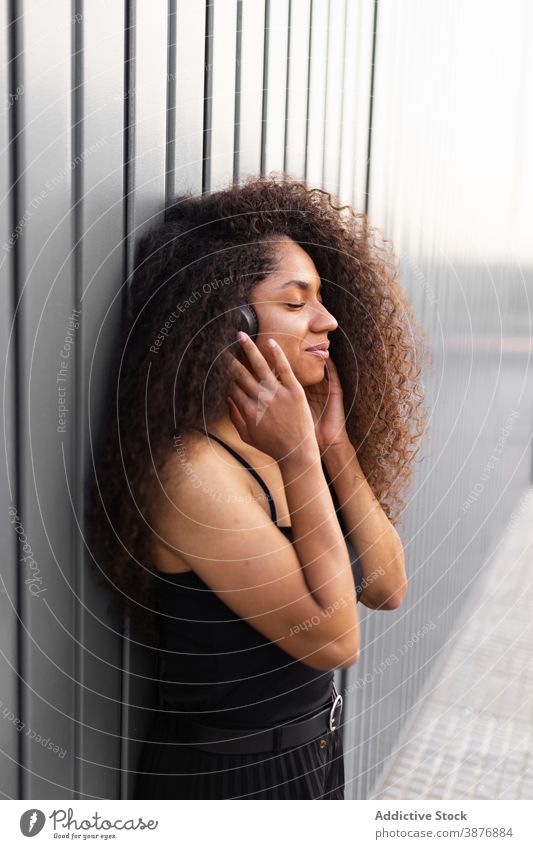 Charmante ethnische Frau mit Kopfhörer auf der Straße krause Haare Afro-Look Frisur charmant Lächeln natürlich Schönheit zuhören schwarz Afroamerikaner