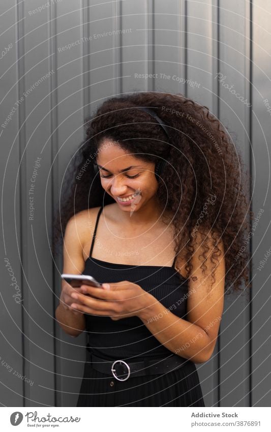 Optimistische schwarze Frau, die auf der Straße Musik hört zuhören Kopfhörer meloman genießen Afro-Look Frisur krause Haare Smartphone ethnisch Afroamerikaner