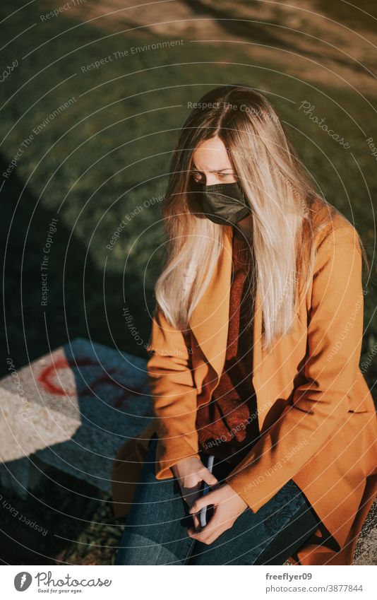 Frau mit Gesichtsmaske auf einer Bank sitzend Sitzen Mantel gelb Winter Herbst betrachtend Vigo Galicia Natur im Freien Sonnenuntergang Kontemplation Himmel