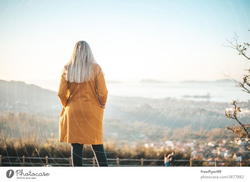 Frau im gelben Mantel sitzt auf einer Bank und betrachtet die Landschaft Winter Herbst betrachtend Vigo Galicia Natur im Freien Freiheit Sonnenuntergang