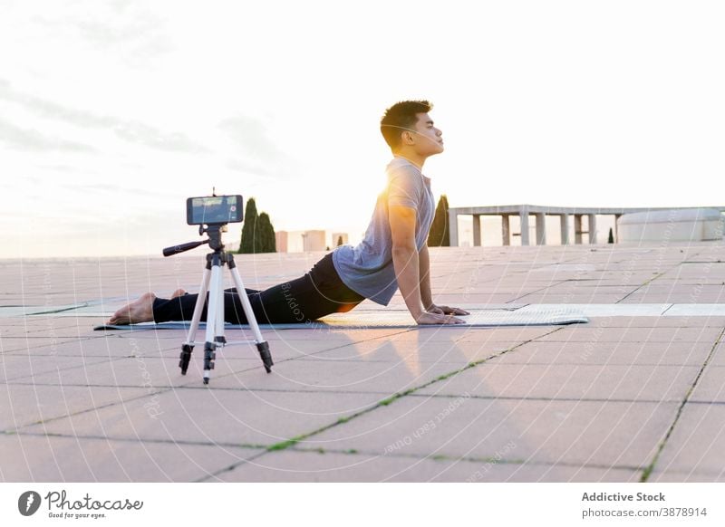 Mann macht Yoga und nimmt Video mit Smartphone auf Aufzeichnen hohe Kobra-Pose Blogger üben bhujangasana Influencer Backend Asana männlich beweglich Lügen