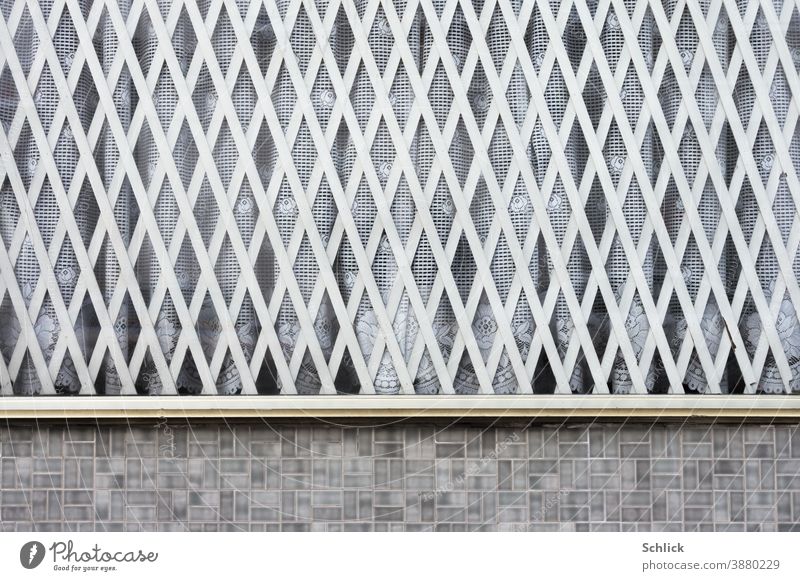 Schaufenster mit hellgrauem Gitter aus Holz und altmodischen Gardinen Holzgitter Rauten vintage Fenster Fassade Außenaufnahme Menschenleer Haus trist Tag