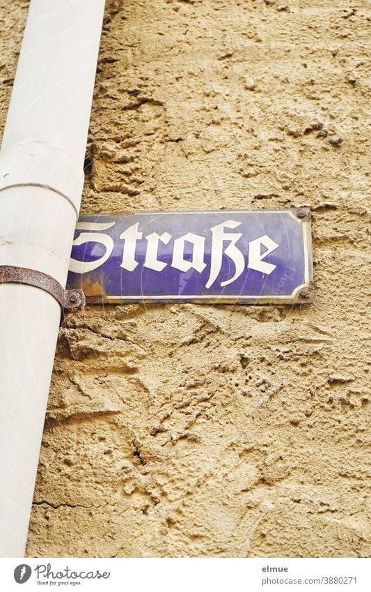 blaues Straßenschild "Straße" klemmt hinter einem Dachrinnenfallrohr an einer grobverputzten Wand Fallrohr Schild Bezeichnung Hinweis Name Straßenname Putz