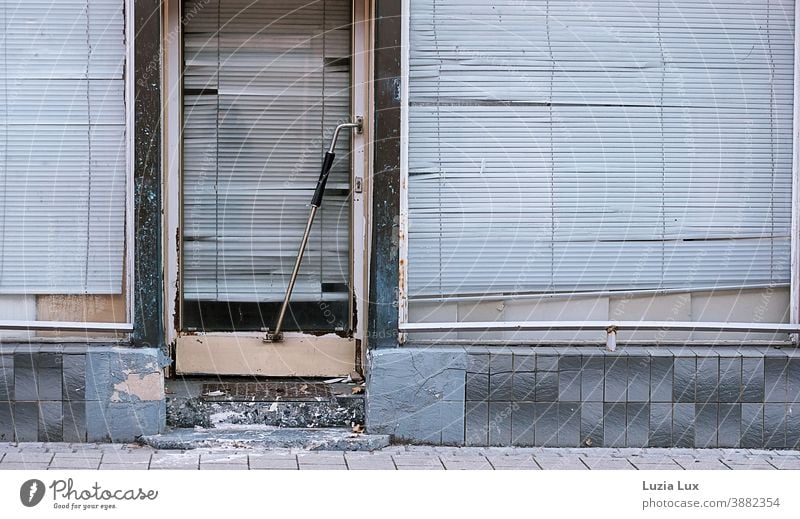 Geschlossen: Straßenansicht eines schon lange geschlossenen Ladengeschäfts mit zerfallenden Eingangsstufen und heruntergelassenen, schiefen Rollos alt baufällig