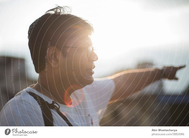 Nahaufnahme des Porträts eines indischen Bengalis mittleren Alters mit Brille in lässiger Stimmung auf dem Dach, mit der Sonne im Rücken als flackerndem Lichtpunkt. Indischer Lebensstil