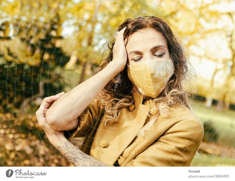 Frau in gelbem Kleid und Maske in einem Park II retuschieren Behaarung Mundschutz Garten Gelblich Blätter Lifestyle reif Porträt eine Person Baum Mantel