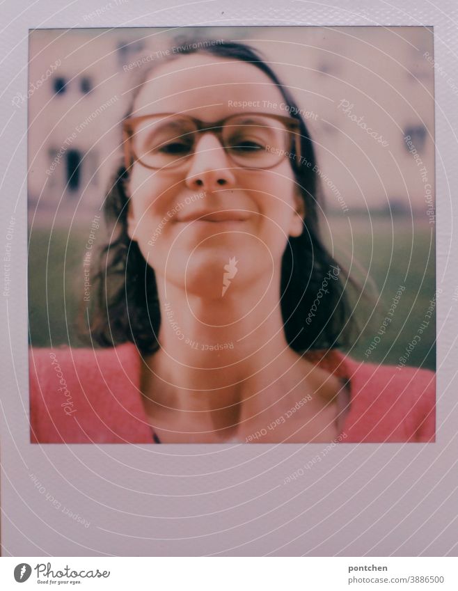 Polaroid-Selfie. Frau mit Brille und braunen Haaren vor einem Haus. Kopf hoch selfie selbstbewusst polaroid lächeln verschmitzt brille Hals gesicht Brünett