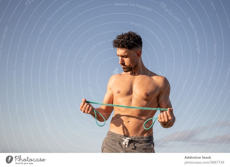 Entschlossener sportlicher Mann beim Training mit Gummiband am Meer Widerstandsband elastisch Bodybuilder Übung MEER Meeresufer nackter Torso stark männlich