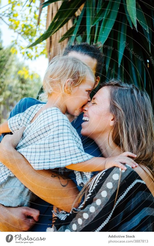 Entzückte Familie umarmt zusammen in tropischen Park Biss Nase Spaß haben Lachen unterhalten heiter Bonden spielerisch Kind Zusammensein Mutter Vater exotisch