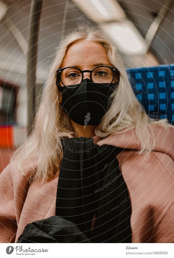 Junge Frau sitzt mit Coronamaske in der Bahn coronavirus junge frau blond lange haare bahn reise gesellschaft winter mantel brille mode style blick hübsch schön