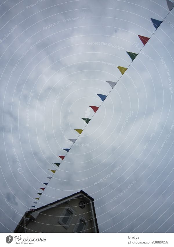 bunte Fähnchen an einer Leine. Straßendekoration Haus Giebelwand, Froschperspektive, bewölkter Himmel, gedeckte Farben Wimpel in einer Reihe