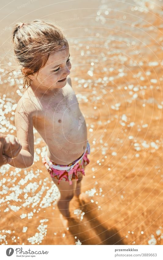 Nahaufnahme eines glücklichen kleinen Mädchens, das im Meer steht und weg schaut und die Hand der Eltern hält oben Erholung niedlich im Freien positiv