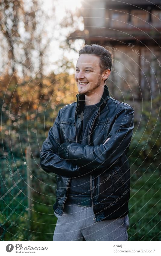 junger Mann in Lederjacke draussen im Freien grün männlich Erwachsener Coolness Oberkörper die Arme verschränkt Profil Junger Mann Freundlichkeit positiv