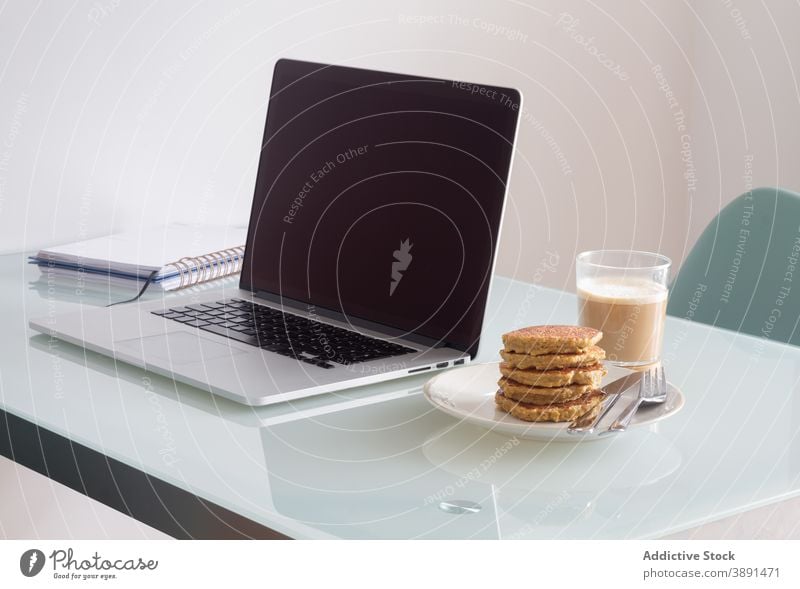 Arbeitsbereich mit servierter Morgenmahlzeit in weichem Licht Arbeitsplatz Küche Tisch Frühstück Kaffee heimwärts Notizblock Laptop Notebook Appartement trinken