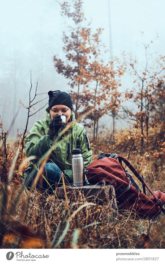 Frau mit Rucksack macht während einer Herbstreise Pause und trinkt am kalten Herbsttag ein heißes Getränk aus der Thermoskanne im Freien Ausflugsziel wandern