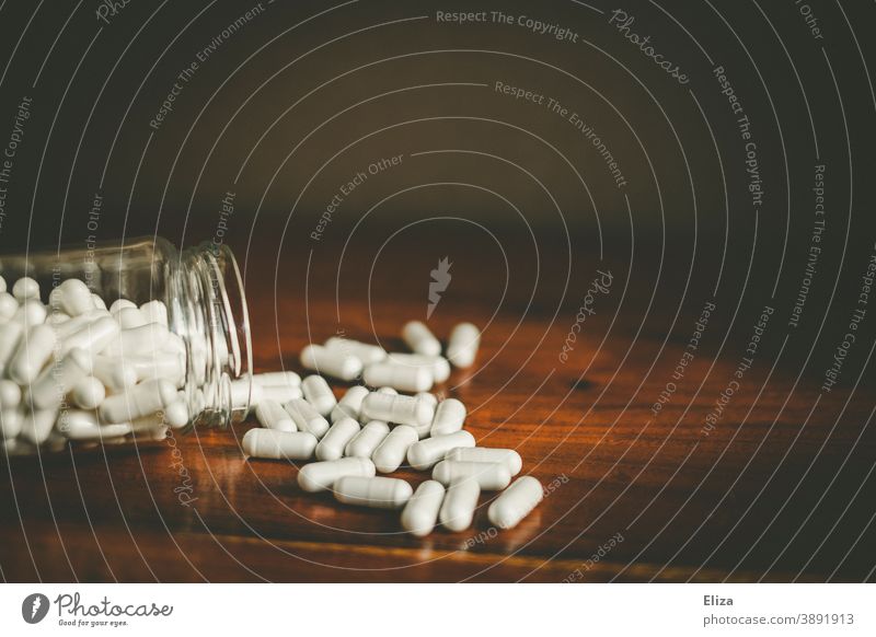 Ein Glas aus dem sich viele weiße Medikamentenkapseln auf einen Tisch ergießen Pillen Medizin Tablette Kapsel Arzneimittel Meidkament Tabletten Vogel Behälter