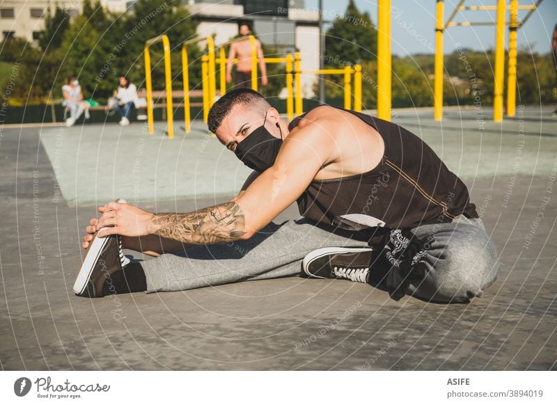 Junger Mann mit Gesichtsmaske, der sich vor dem Training der Gymnastik dehnt calisthenics Sport Aufwärmen strecken Athlet Mundschutz Coronavirus neue Normale