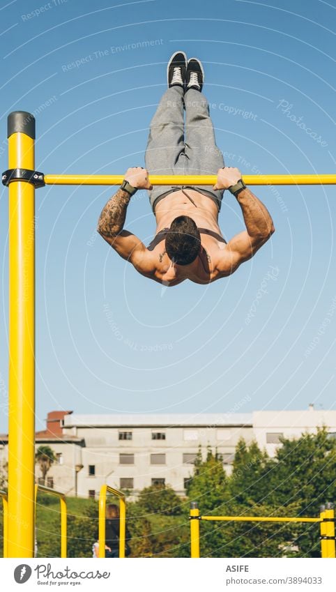 Junger athletischer Mann turnt am Barren in einem Gymnastikpark calisthenics Sport Athlet Muskeln Stärke Kunstturnen Straße Freestyle pirouettieren herumwirbeln