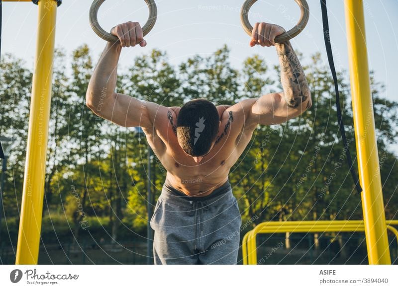 Athletischer junger Mann beim Vorbereiten und Kontrollieren von Gymnastikringen calisthenics Sport Ringe Muskeln Stärke Kunstturnen Straße Freestyle Körper