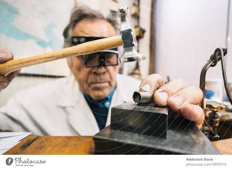 Juwelier mit Hammer und Meißel beim Erstellen von Schmuck in der Werkstatt Beitel Edelstein Arbeit professionell Mann Werkzeug Fähigkeit reif männlich Meister