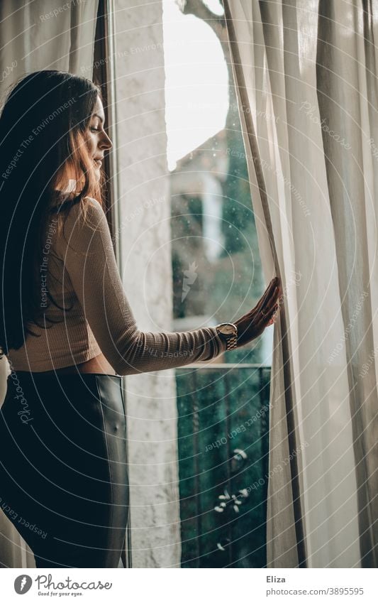 Junge Frau steht am Fenster und beobachtet die // Nachbarschaft Blick aus dem Fenster Vorhang rausschauen Fensterscheibe Sehnsucht zuhause bleiben beobachten