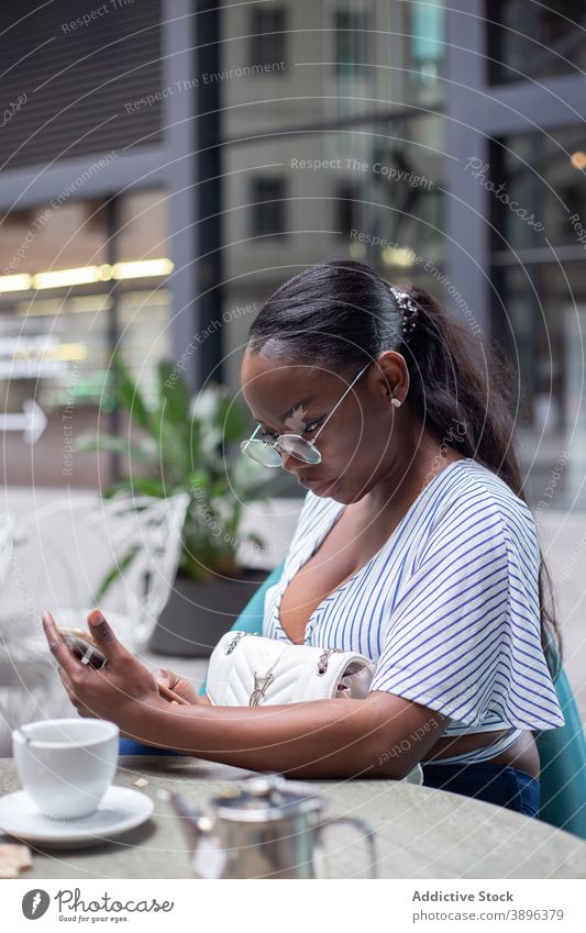 Ethnische Frau entspannt in Café auf Smartphone Tee Teekanne ruhen sorgenfrei Apparatur Gerät ethnisch schwarz Browsen Handy Afroamerikaner Kälte Tisch