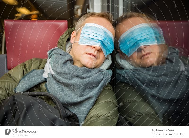 Reisen in öffentlichen Verkehrsmitteln während der Pandemie. Ein müder Mann mittleren Alters mit einer medizinischen Schutzmaske auf dem Gesicht schläft im Nahverkehrszug.