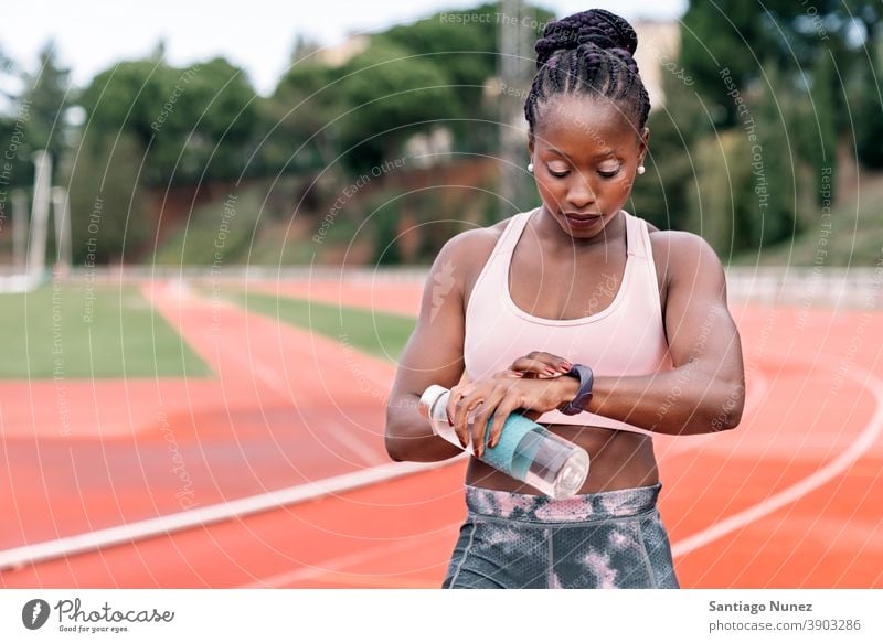 Athlet Sprinter beobachten die Uhr mit einer Flasche Wasser Zeit Start Rennen Training Krawatte Hydratation ethnisch Afro-Look afroamerikanisch Bahn Zug