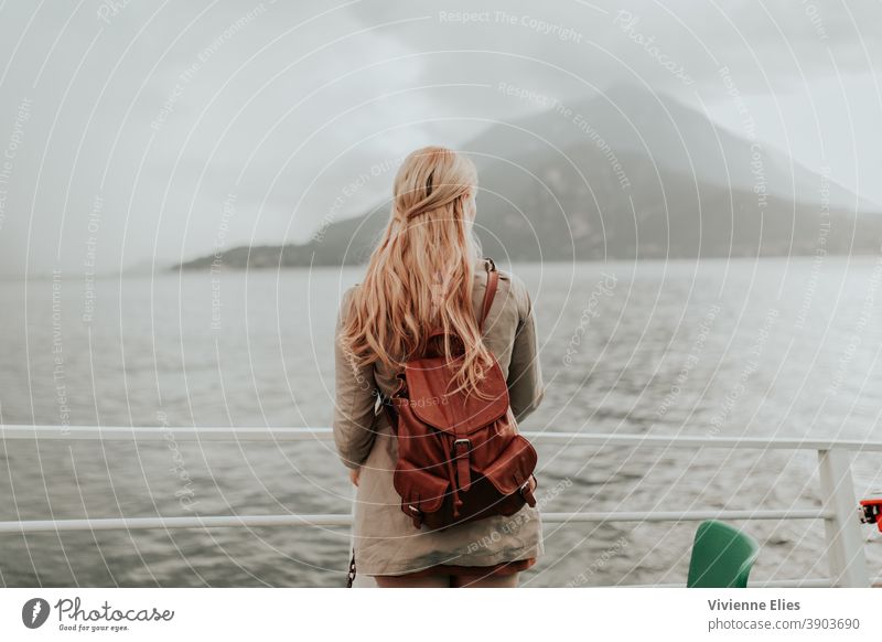 Frau steht mit einem Rucksack auf einem Boot blond lange Haare elegant schwarzes Kleid Meditation entspannend Natur Wasser See Fluss Baden baden Denken