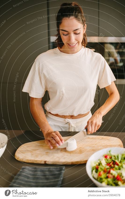 Lächelnde Frau Schneiden von Käse für Salat in der Küche Feta geschnitten Salatbeilage vorbereiten Koch Gemüse lecker heimwärts selbstgemacht Messer Gesundheit