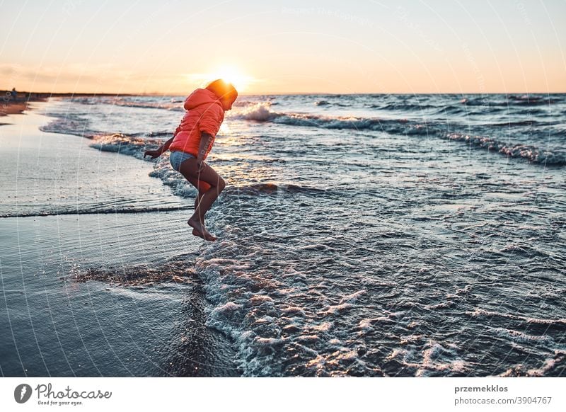 Verspieltes kleines Mädchen, das bei Sonnenuntergang am Sandstrand über die Meereswellen springt aufgeregt frei genießen positiv Emotion sorgenfrei Natur