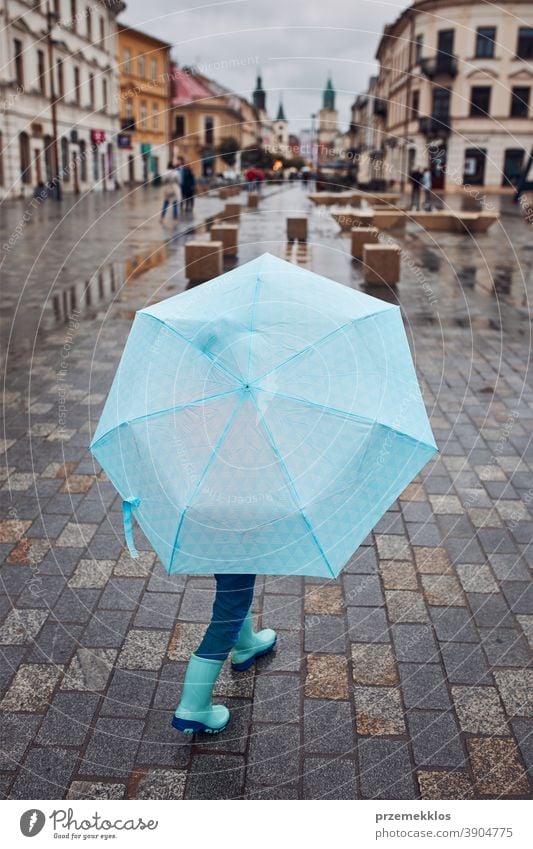 Kind hält großen blauen Regenschirm in der Hand und geht an einem verregneten, düsteren Herbsttag durch die Innenstadt im Freien wenig saisonbedingt fallen