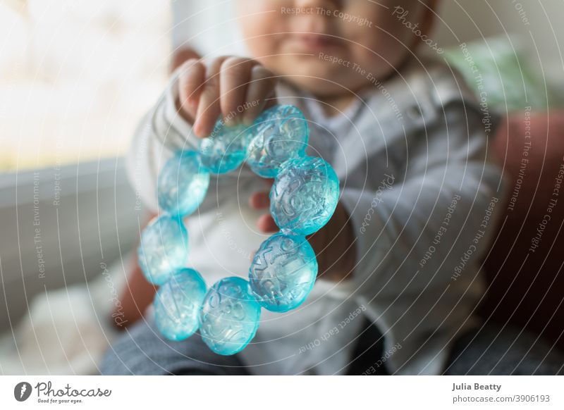 6 Monate altes Baby hält einen blauen Beißring in den Händen zahnend Kauen Zähne sechs Monate Säugling Halt packen erkunden sensorisch Wasser kalt Kunststoff