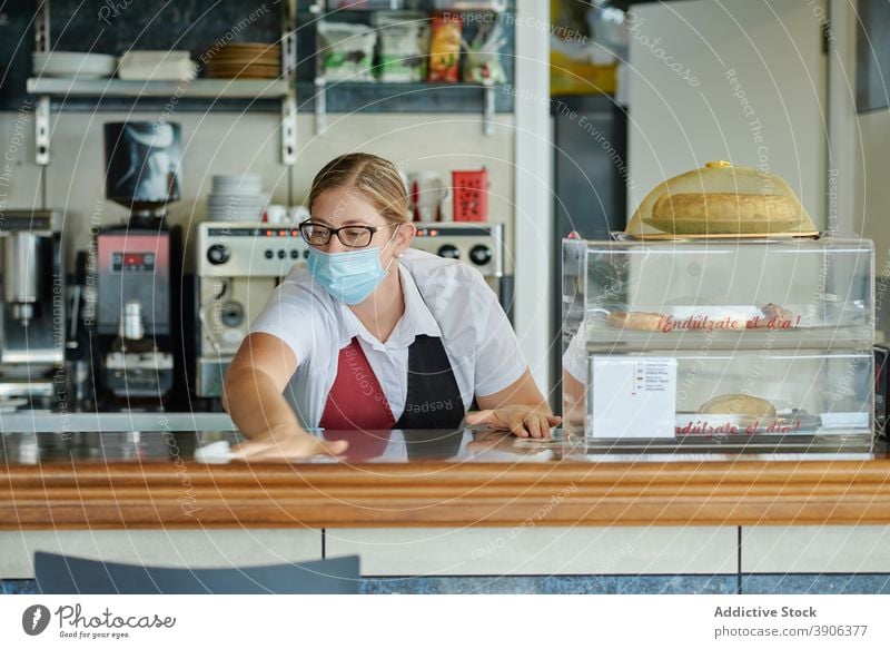 Barista desinfiziert Theke in Cafeteria Coronavirus Kantine desinfizieren Abfertigungsschalter Sauberkeit Barkeeper Arbeit Hygiene Mundschutz Pandemie Frau