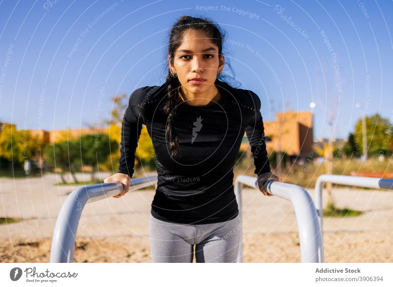 Fitte Frau macht Übungen am Parallelbarren auf dem Sportplatz Trizeps parallel Bar calisthenics Training Gleichgewicht Pumpe stark ethnisch schlank