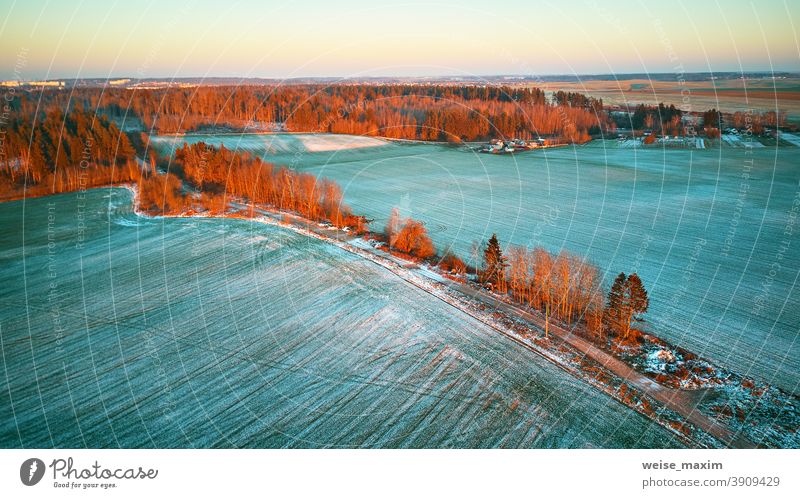 Bunte Bäume im Dezember Sonnenuntergang Luftaufnahme. Ländliche Schotterstraße. Draufsicht auf die Landschaft. Feld Schnee Winter Ernte Antenne Ackerbau Straße