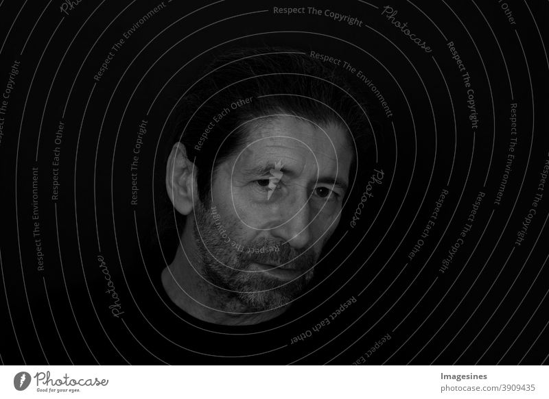 Schwarzweiss Porträt des bärtigen Mannes mit einem kritischen und ernsten Ausdruck auf dunklem schwarzem Hintergrund. Porträt des denkenden wütenden Mannes.