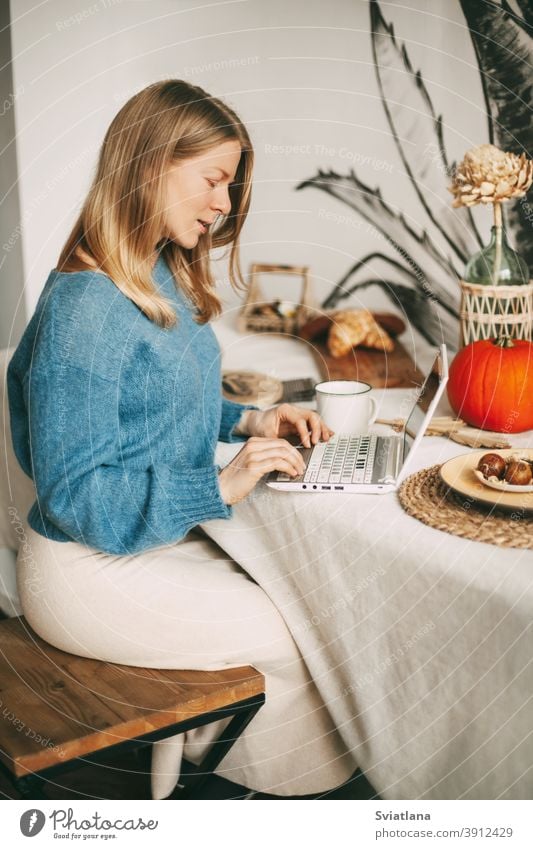 Nettes blondes Mädchen, das am Morgen an einem Laptop arbeitet und Kaffee trinkt. Arbeit online, freiberuflich, soziale Distanz benutzend schön Küche Frau