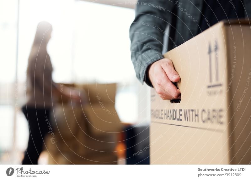 Close Up Of Man Carrying Removal Box As Couple Move In Or Out Of New Home Paar junges Paar Hauskauf Verpackung ausrückend Umzug Aufrüstung tragen Kasten