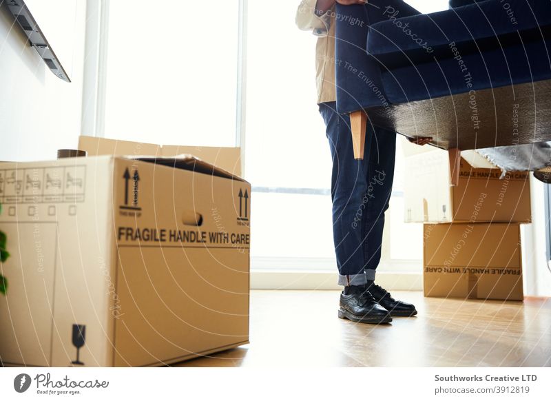 Close Up Of Man In New Home Carrying Sofa in Lounge On Moving Day Surrounded by Umzugskartons Mann junge Männer Hauskauf tragen Heben Möbel Wohnzimmer räkeln